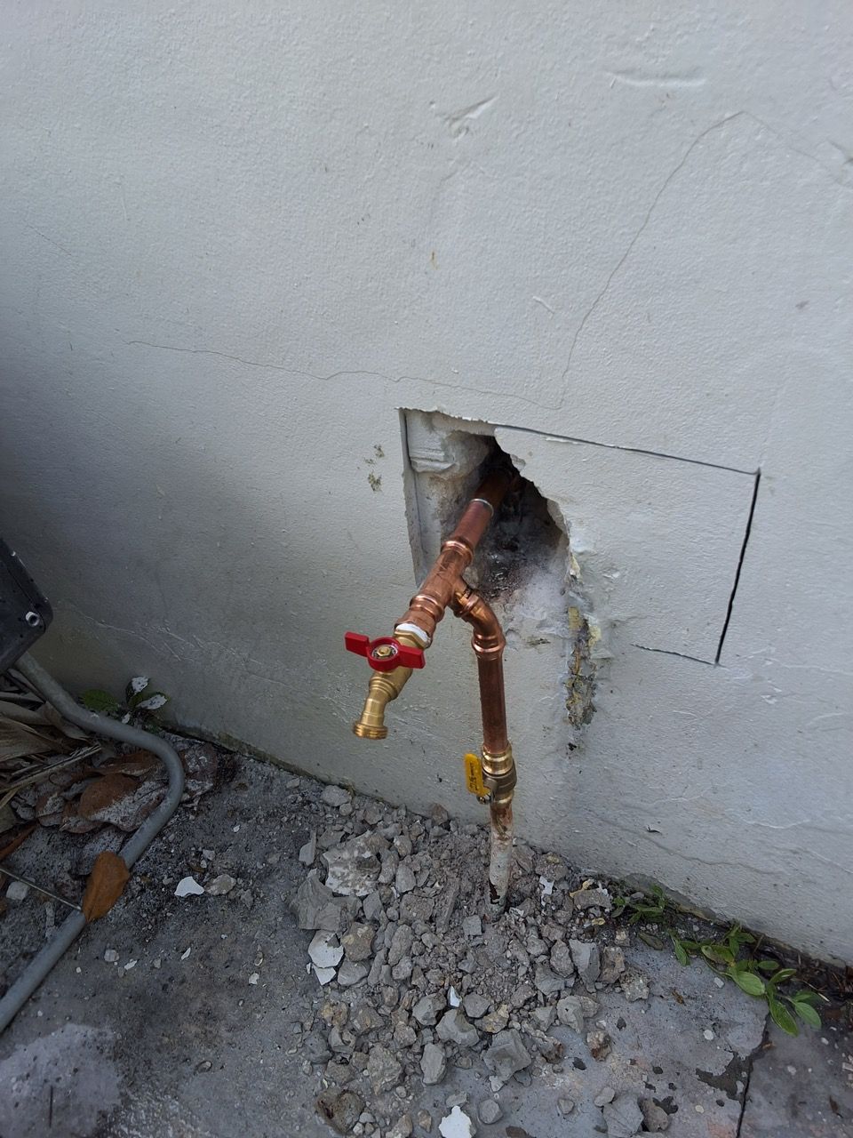 Broken exterior wall with exposed copper pipes and red/yellow valves near the ground
