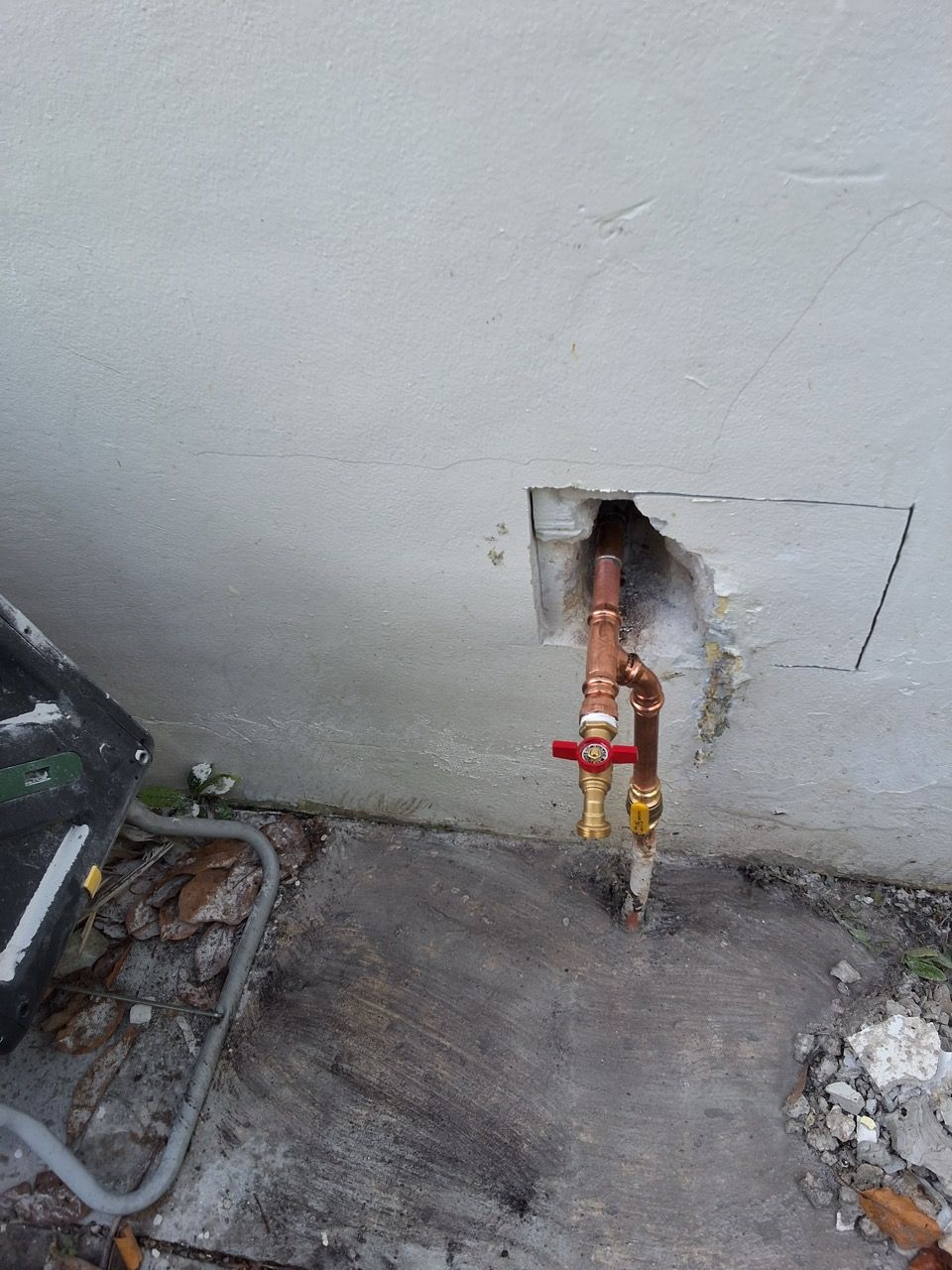 Outdoor wall with exposed red and yellow gas pipes near the ground, beside concrete and debris.