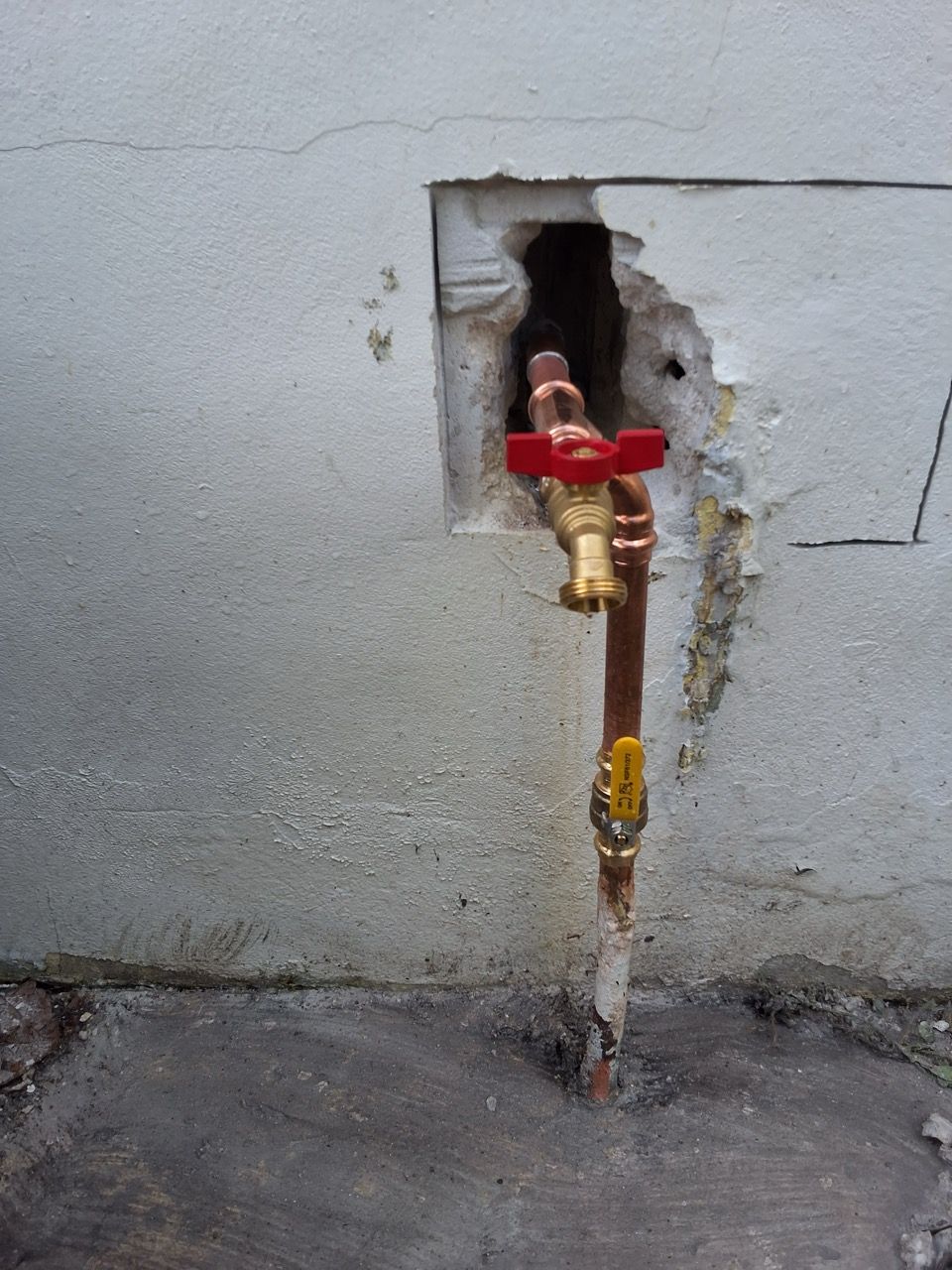 Red water shutoff valve and brass pipe protruding from a hole in a gray wall.