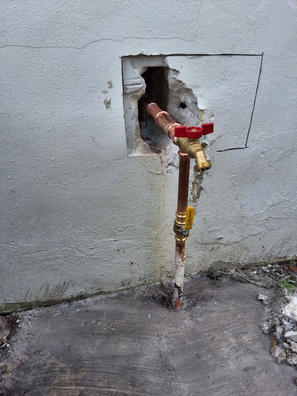 Exposed water pipe with red valve protruding from a hole in a gray wall