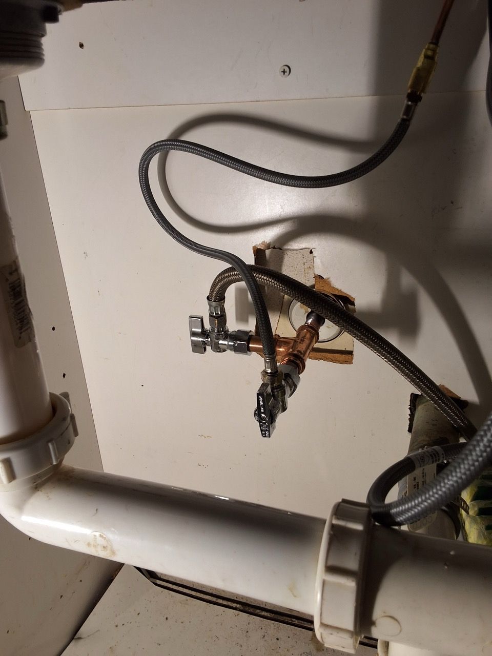 Under-sink plumbing with hoses, valves, and a white drain pipe inside a cabinet.