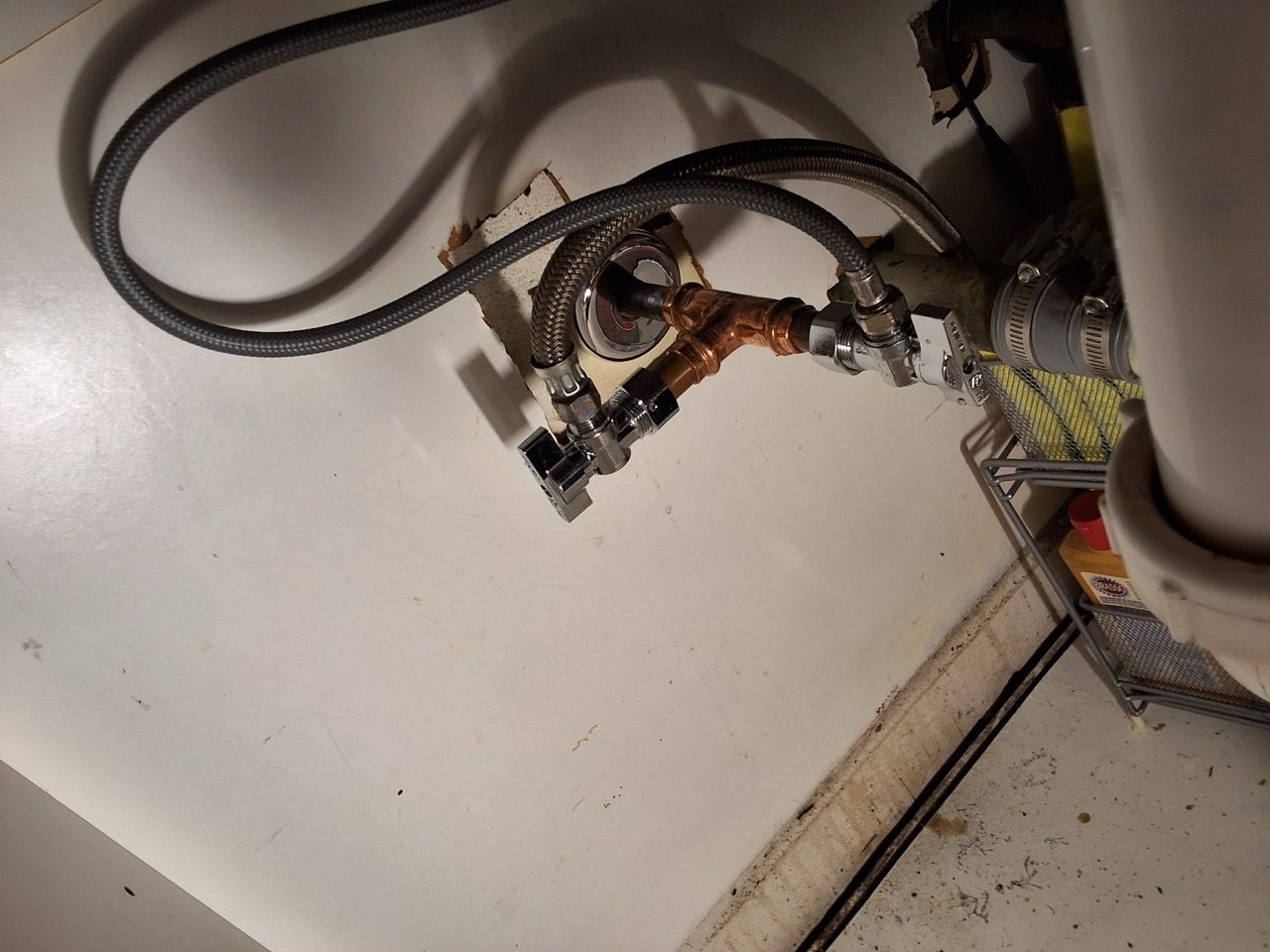 Close-up of bent copper pipes and electrical cables inside a utility panel.