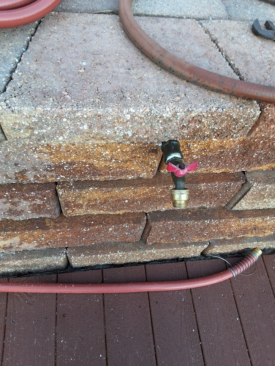Outdoor brick wall with a small black-and-pink faucet and a red hose on the ground.