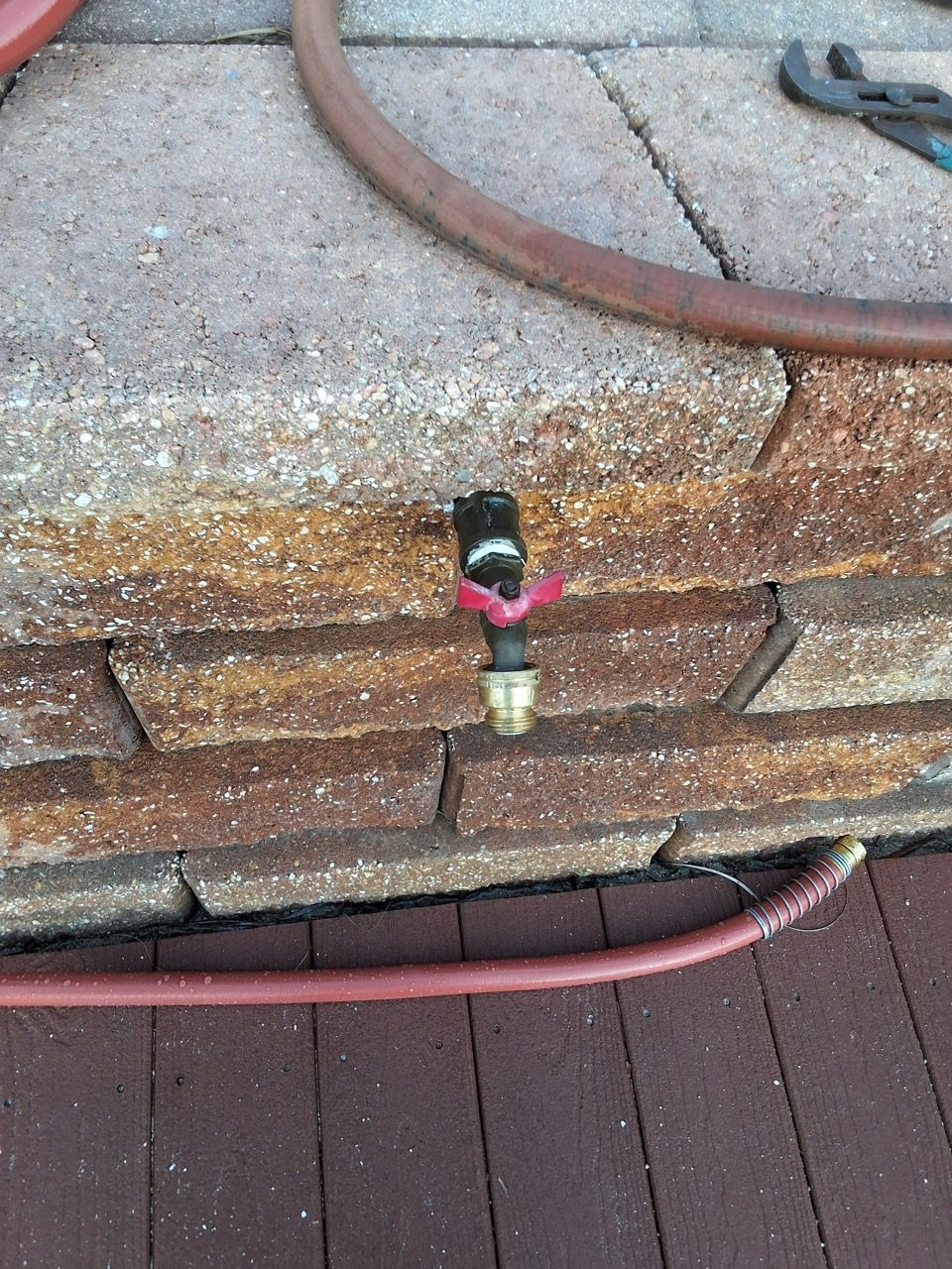 Brick wall with a hose bib and red garden hose on a wooden deck