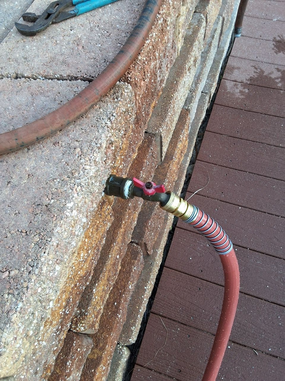 Close-up of a garden hose connection attached to a weathered concrete edge
