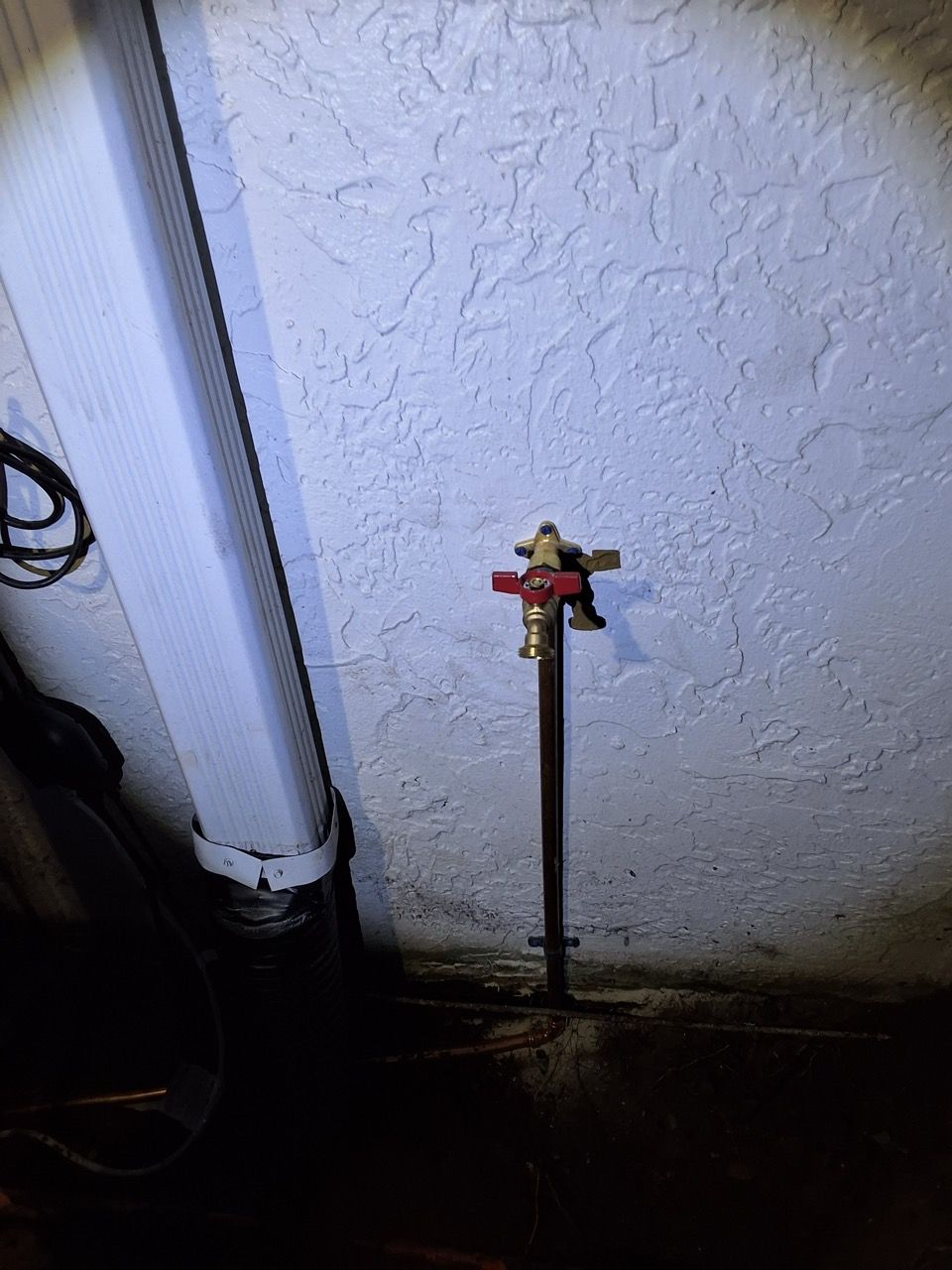 Outdoor water shutoff valve on a black pipe beside a textured white wall.