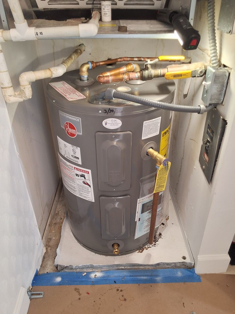 Cylindrical water heater in a utility closet with pipes, valves, and warning labels