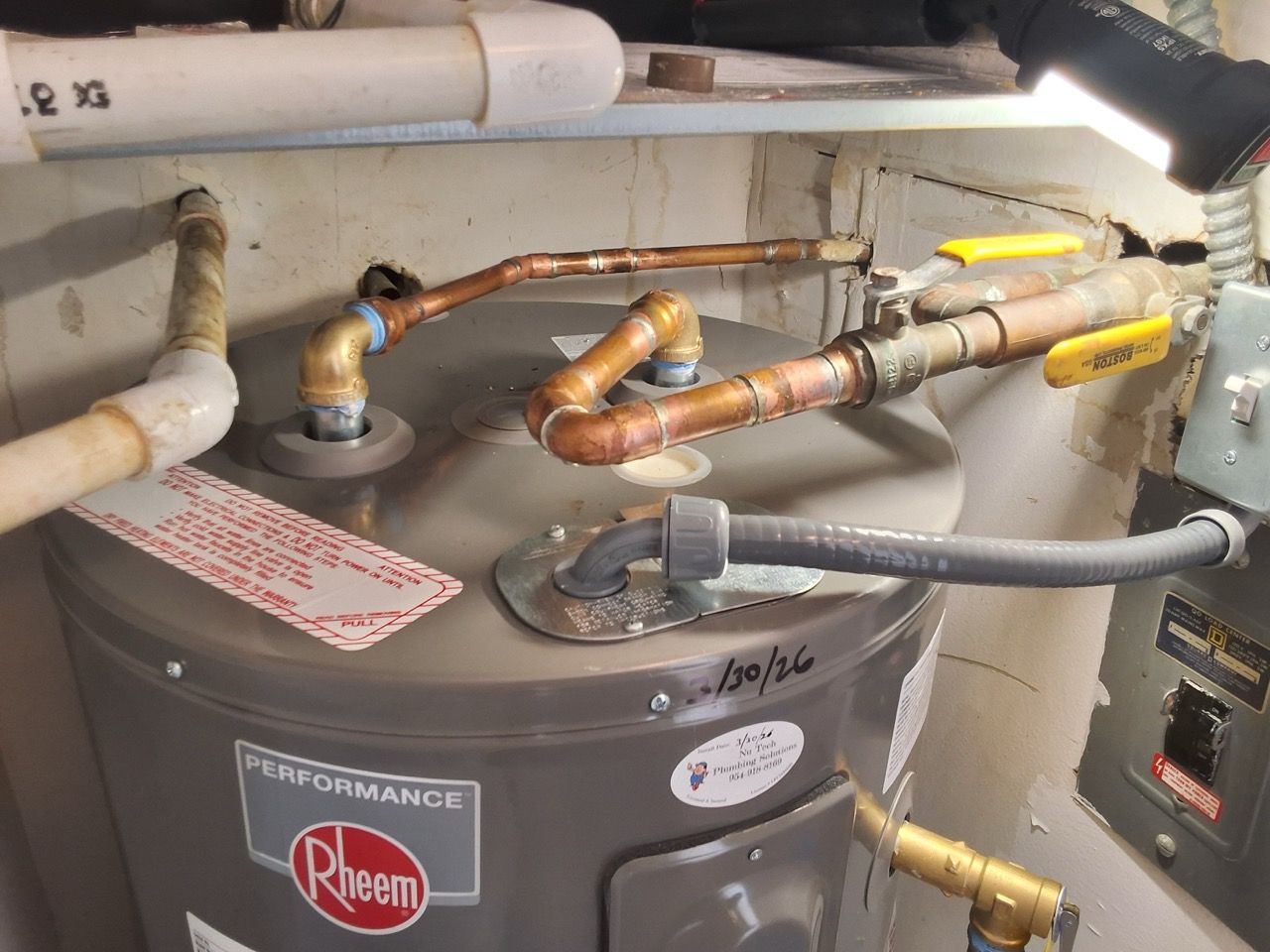 Water heater with copper pipes, valves, and yellow-handled shutoff levers in a utility room.