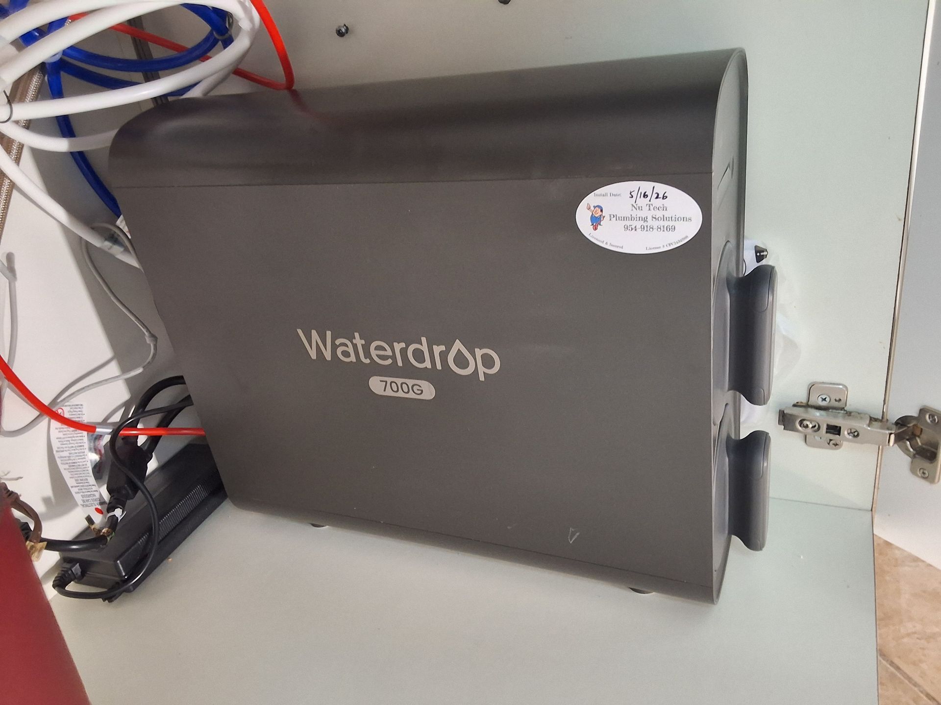 Wall-mounted gray Waterdrop appliance with connected hoses and wires in a utility space