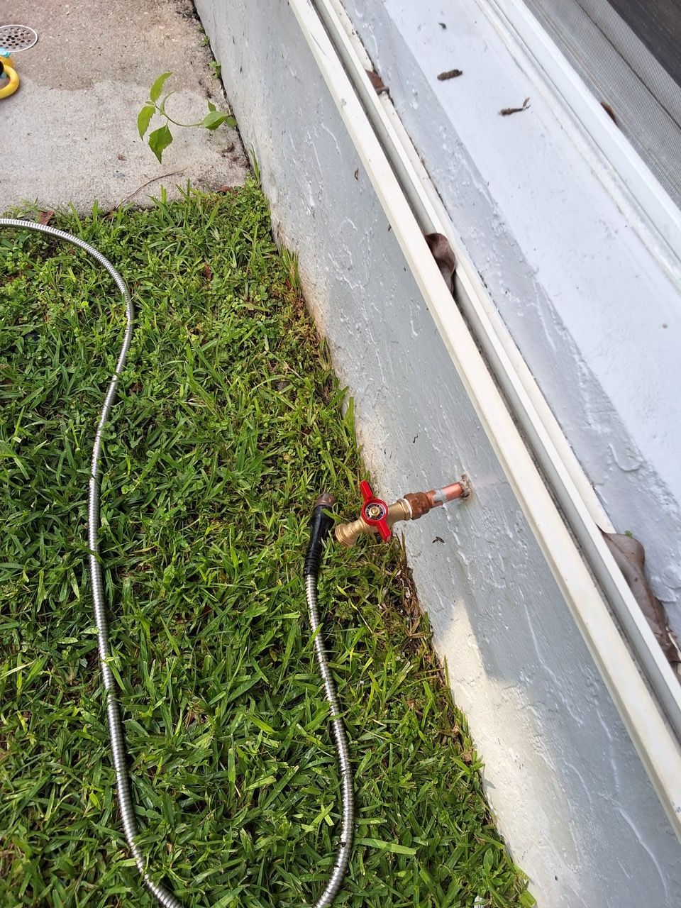 Red hose bib on gray wall beside grass, with a black cord lying across the lawn.