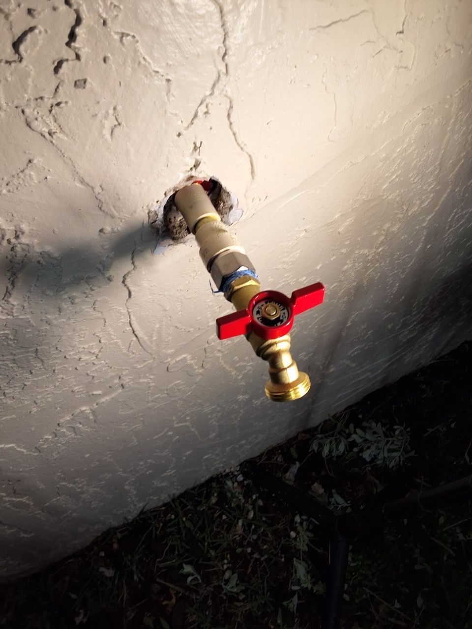 Water shutoff valve with red handle protruding from a wall pipe at night