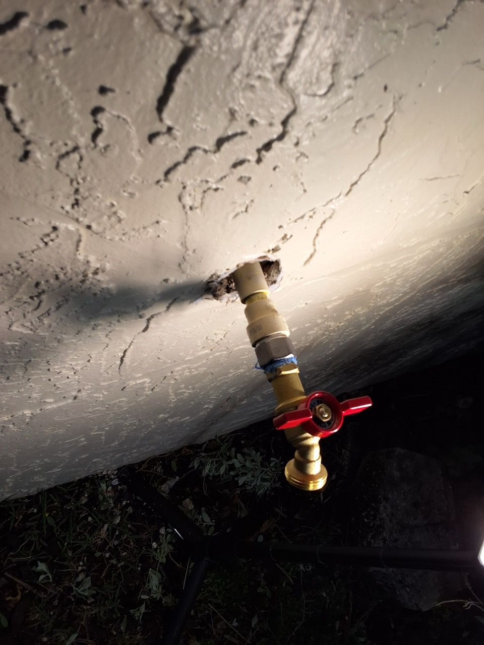 Outdoor faucet with a red handle mounted on a concrete wall at night