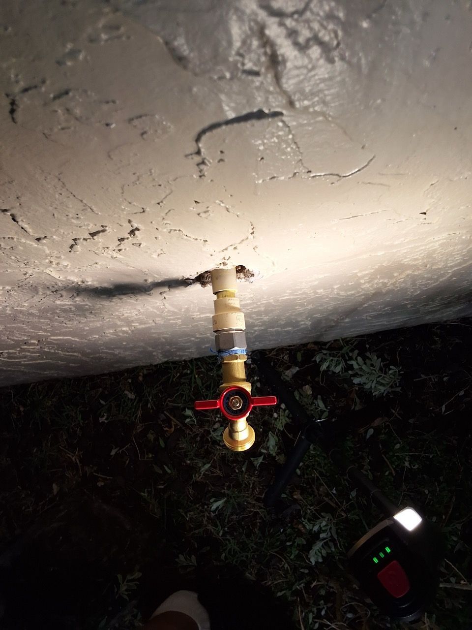 Close-up of an outdoor water shutoff valve on a ceiling, with red handle and pipes visible.