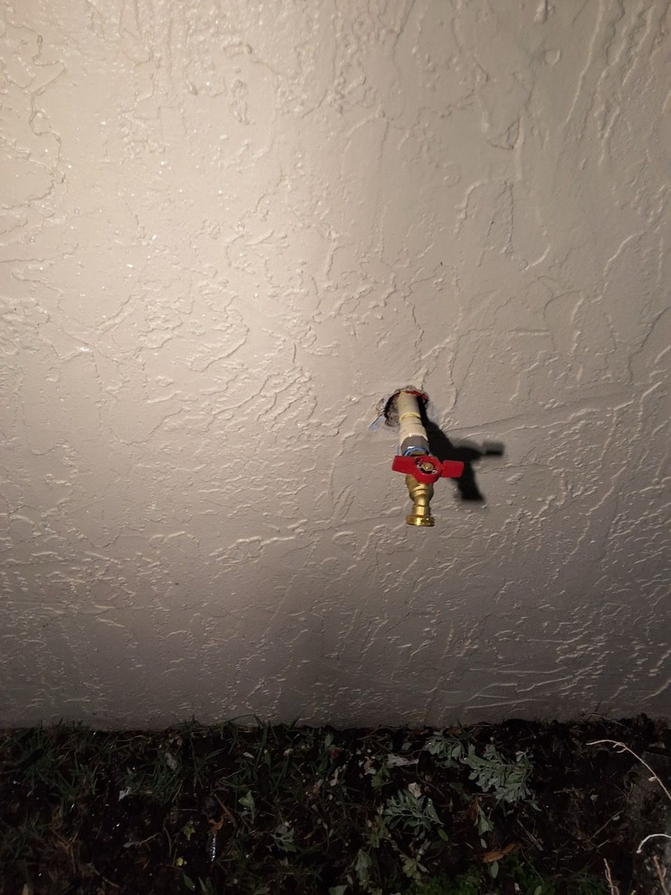 Small toy figure in red and black hanging on a textured wall above dark foliage
