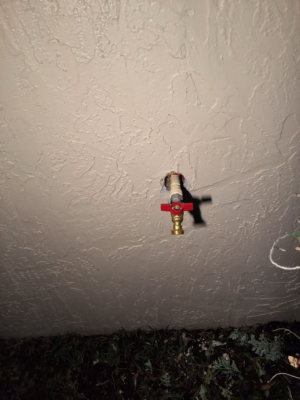 Small sprinkler head mounted on a textured ceiling, with a red valve and dark debris below.