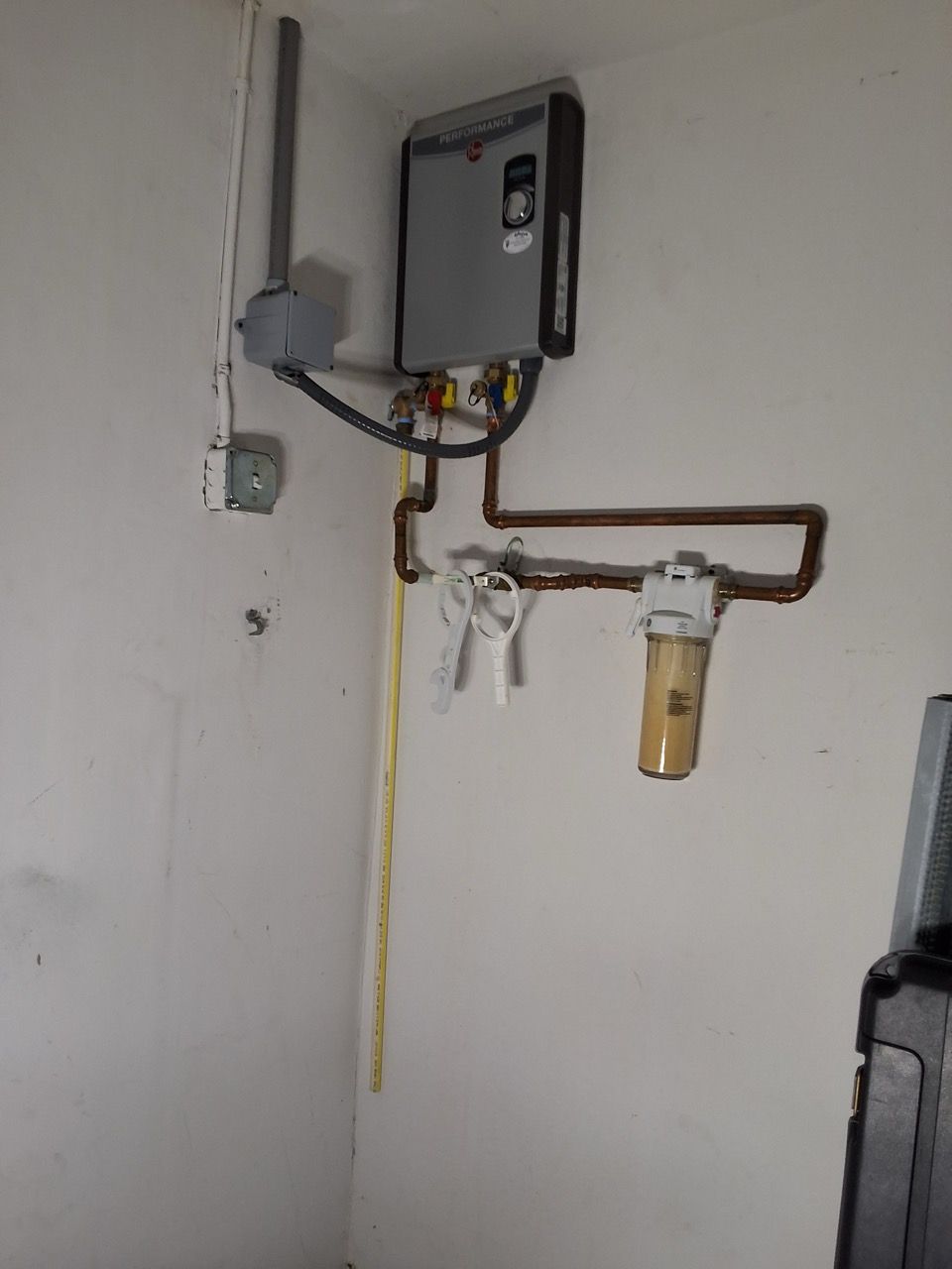 Wall-mounted utility equipment and pipes on a white wall, including a gray box and a small filter canister.