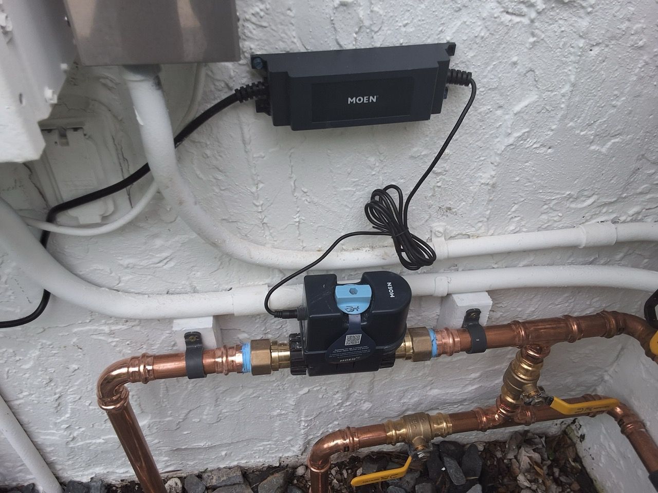 Copper pipes with a black valve and blue handle mounted against a white wall, with cables above.