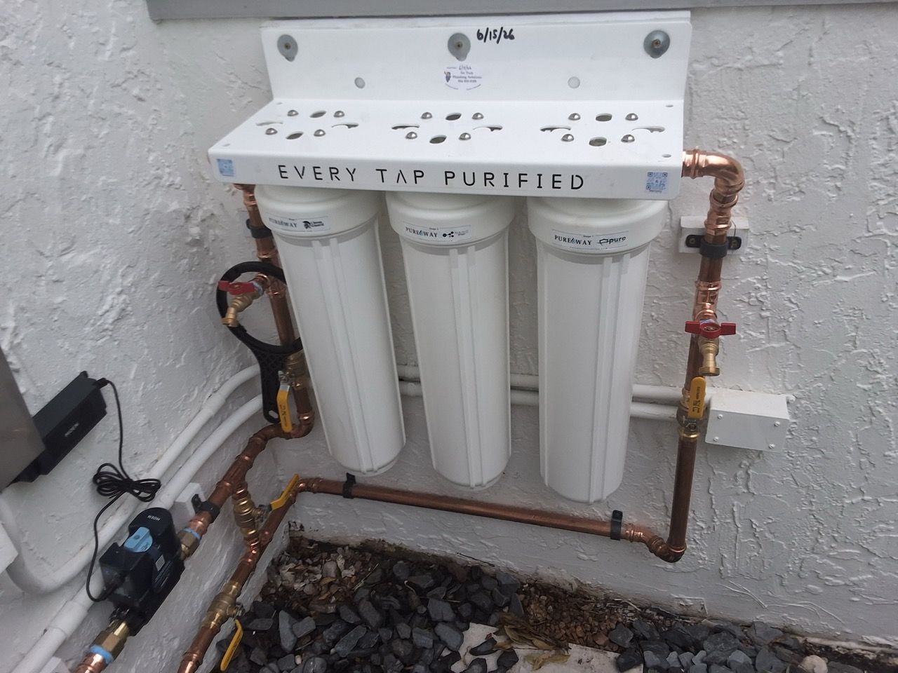 Under-sink water filtration system with three white filter canisters and exposed copper piping.