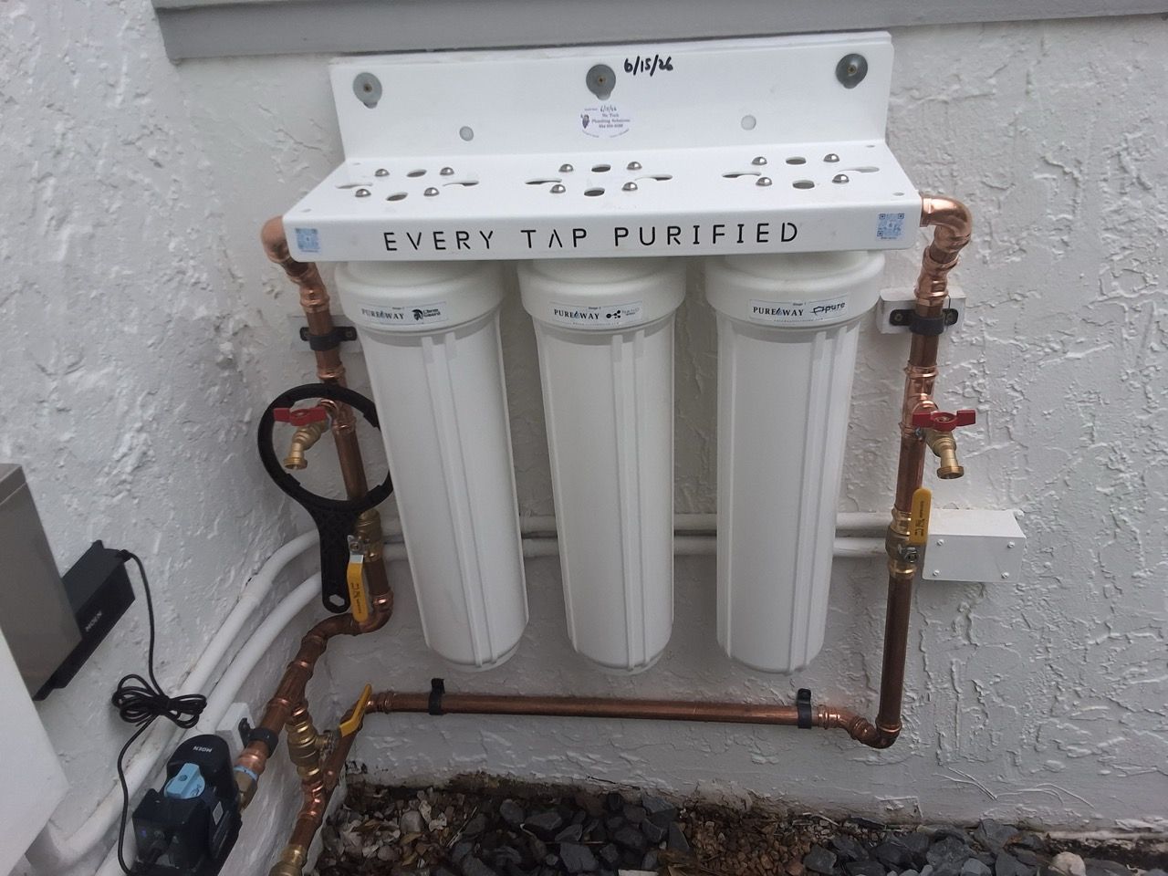 Three white water filter cartridges mounted under a countertop with copper plumbing and valves