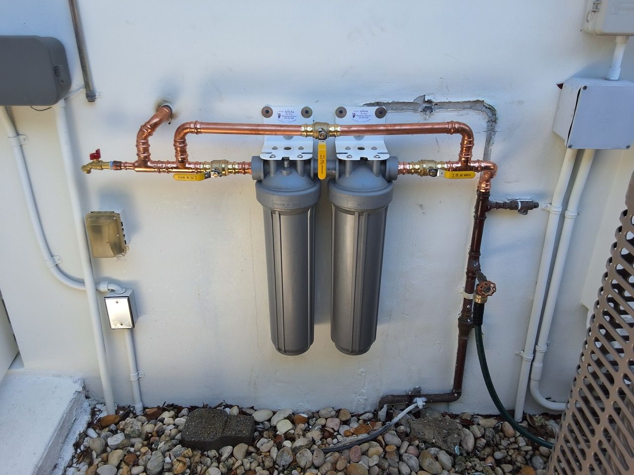 Two wall-mounted water filter canisters with copper pipes in a utility area.