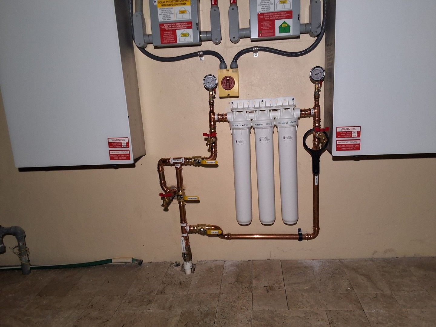 Water filtration system with pipes and valves mounted between two wall units in a utility room