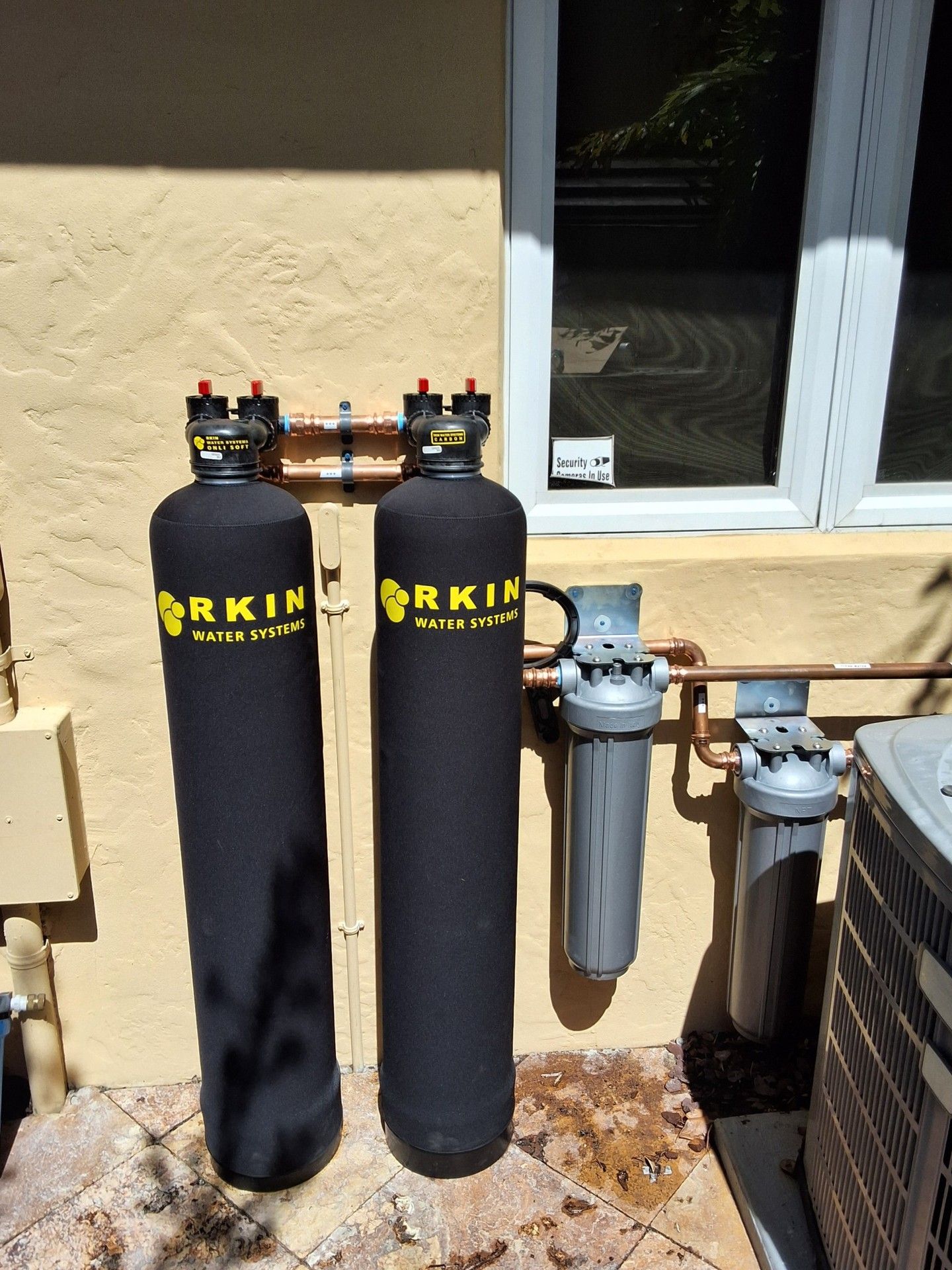 Two black water filtration tanks beside a house exterior wall and utility meters