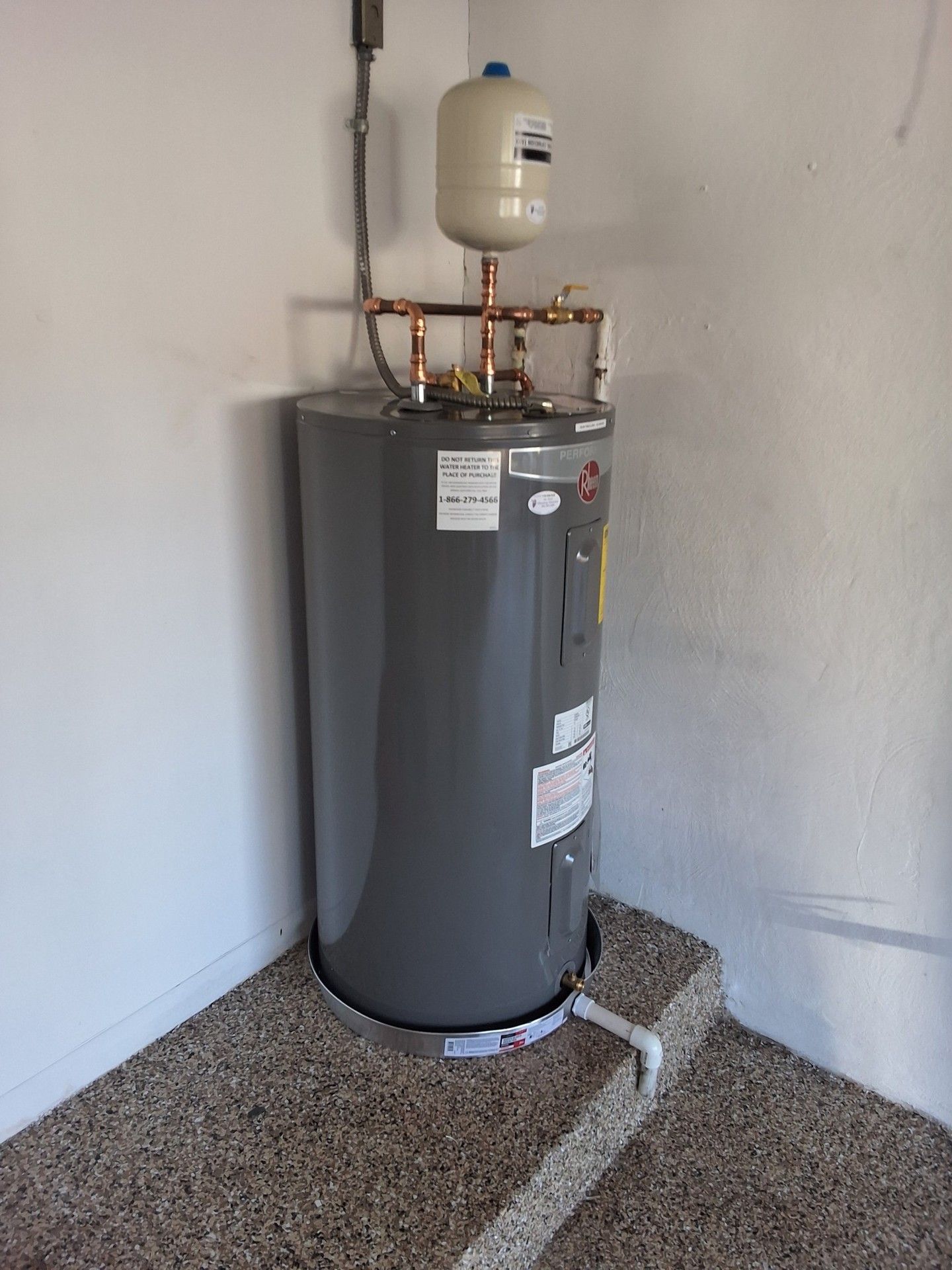 Gray water heater with pipes and expansion tank in a utility room corner.