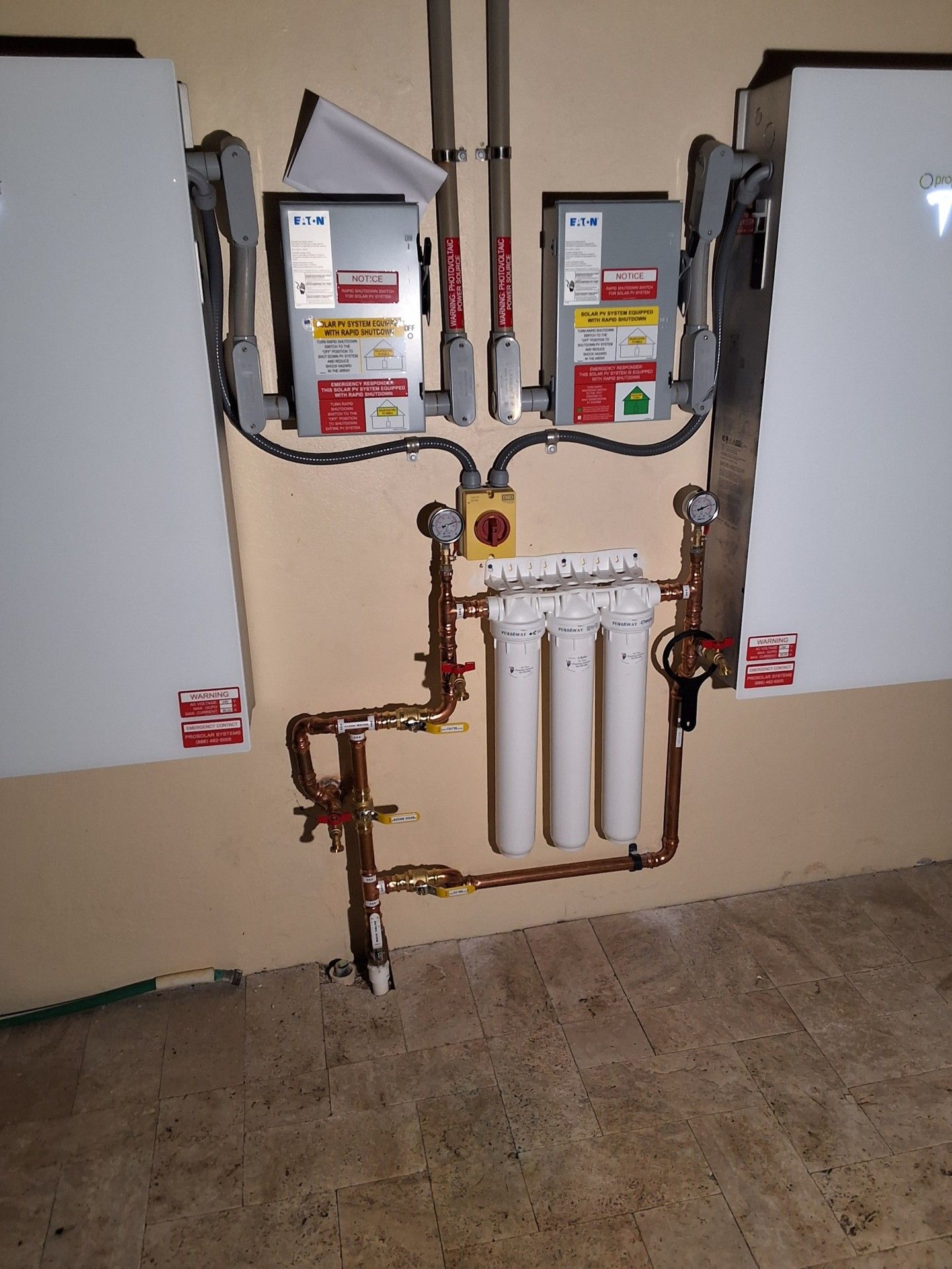Two wall-mounted water heaters with exposed copper piping and valves in a utility room