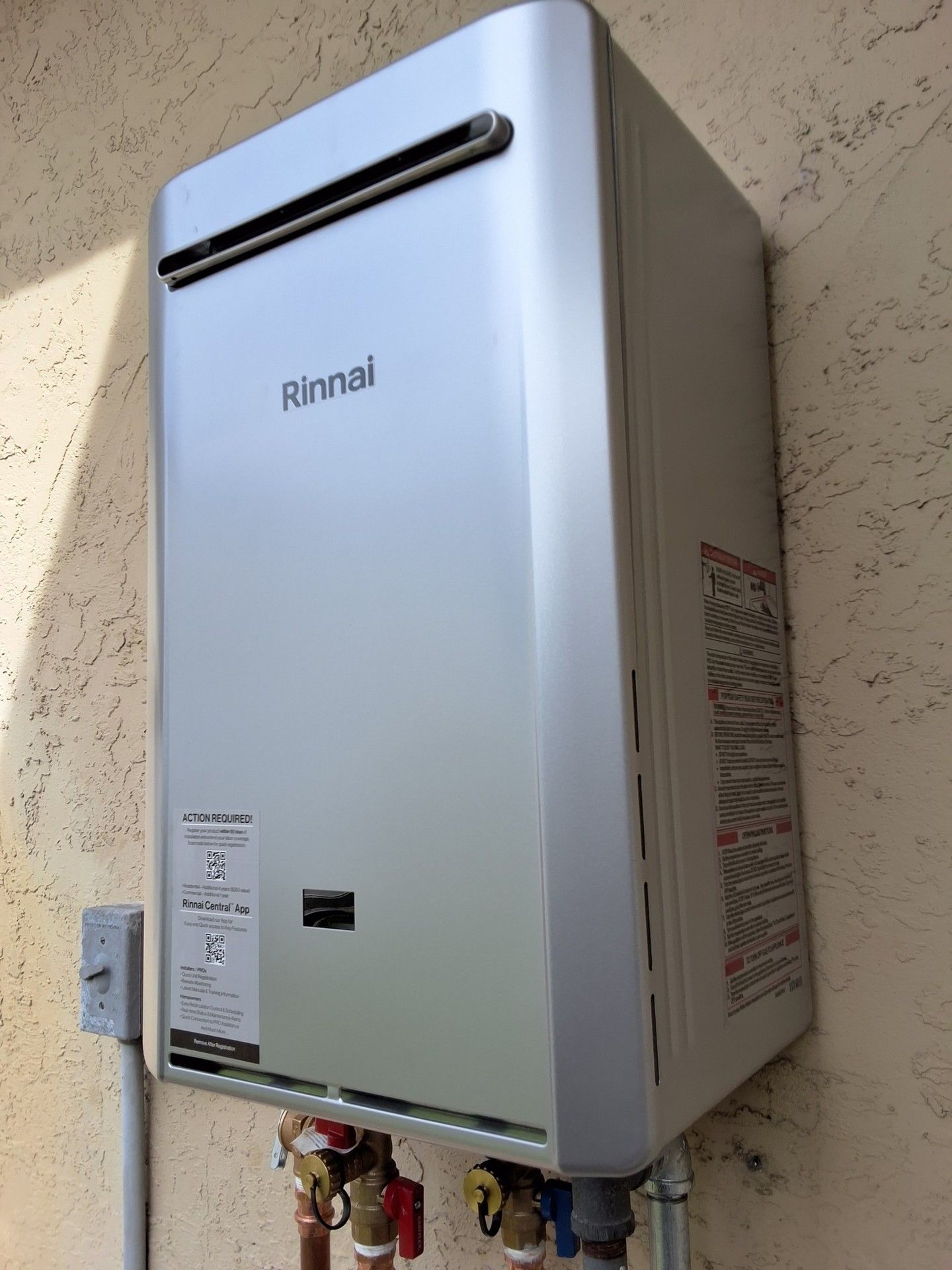 Wall-mounted white Rinnai tankless water heater with exposed pipes on an exterior wall