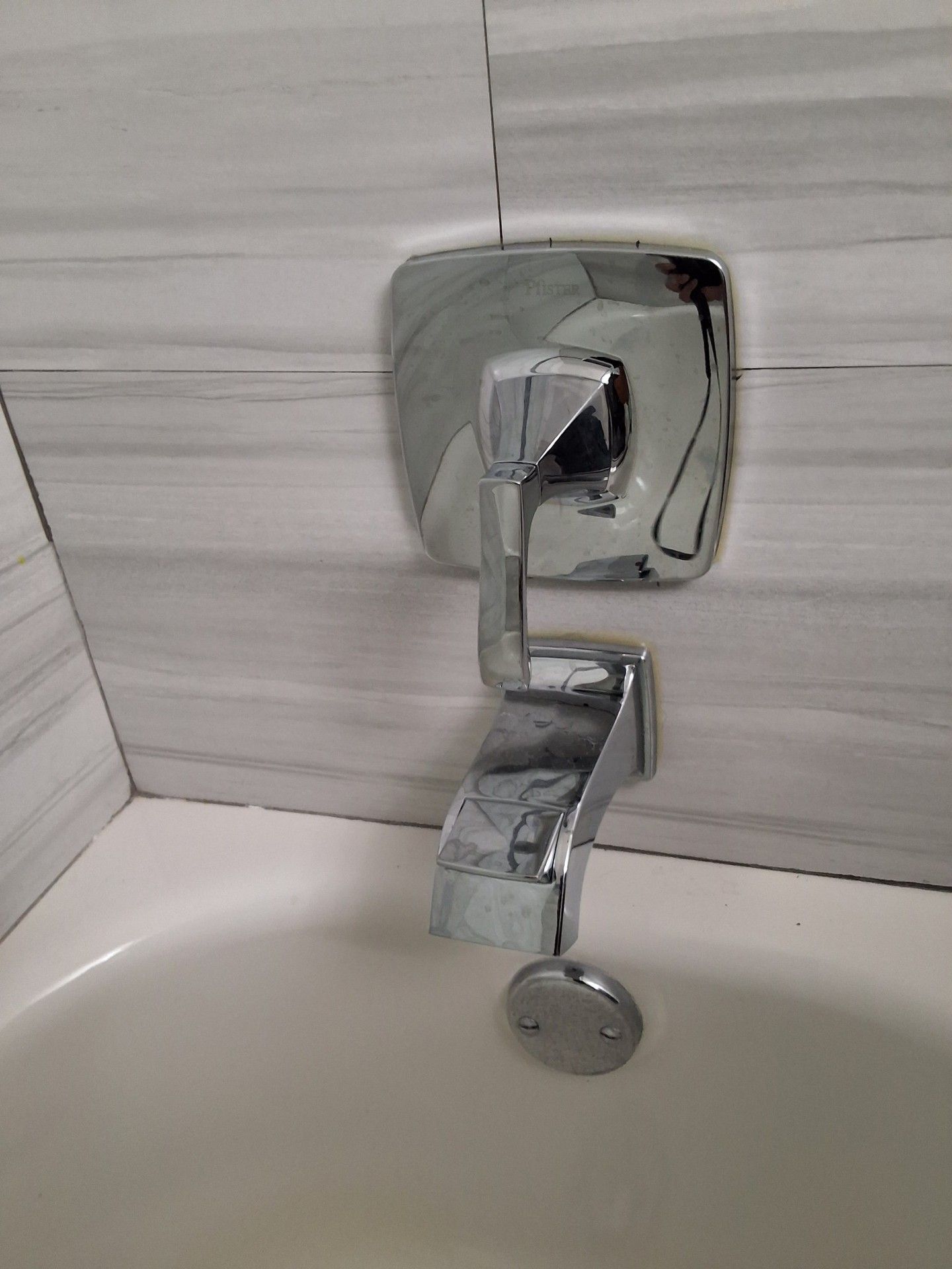 Chrome bathtub faucet with lever and round drain control against white tile wall