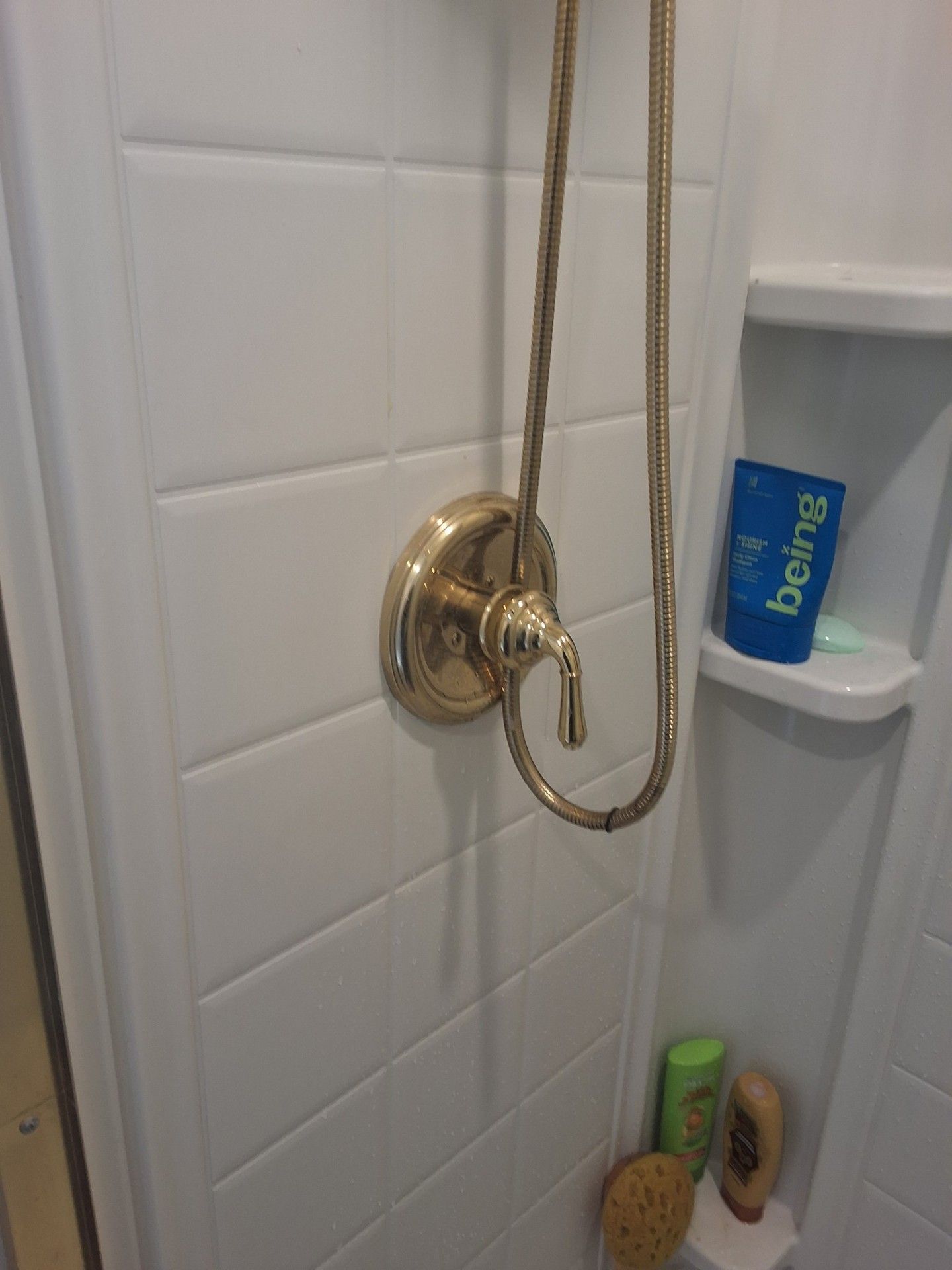Brass shower valve and hose in a white tiled shower with a blue soap box on a corner shelf