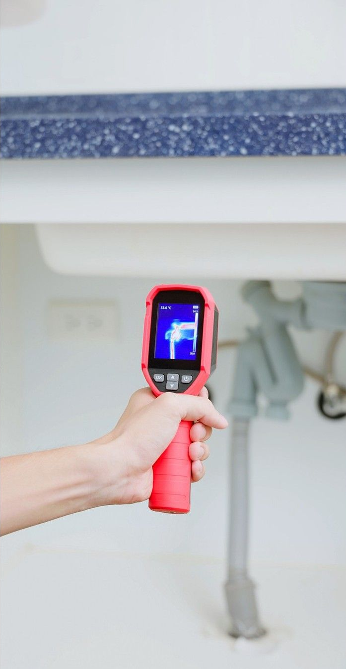 Handheld thermal camera aimed under a countertop, showing heat image on screen