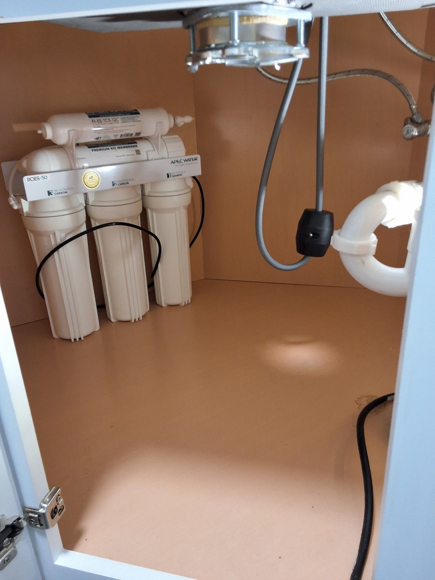Under-sink water filter system with white canisters and hoses inside a cabinet