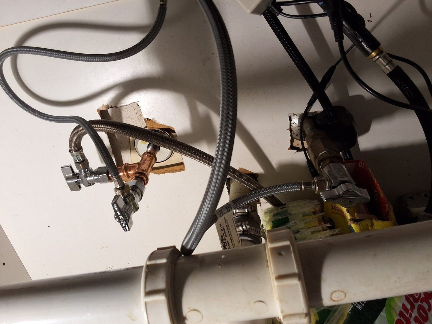 Plumbing pipes and flexible hoses under a sink with valves and fittings.