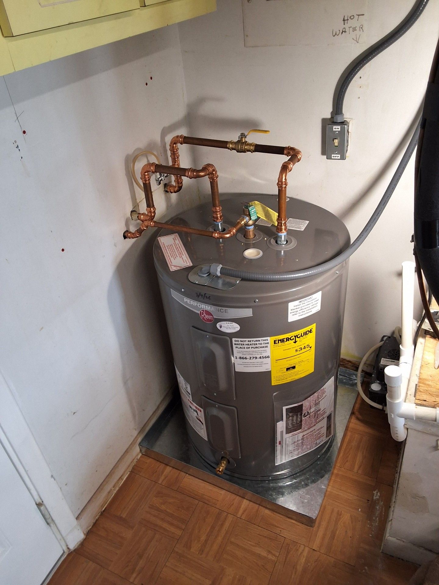 Water heater with copper pipes in a utility closet beside a wall and door.