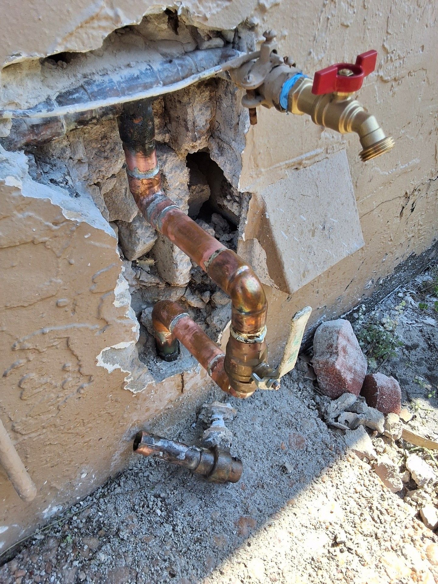 Exposed copper pipes and a red-handled valve protruding from a wall exterior