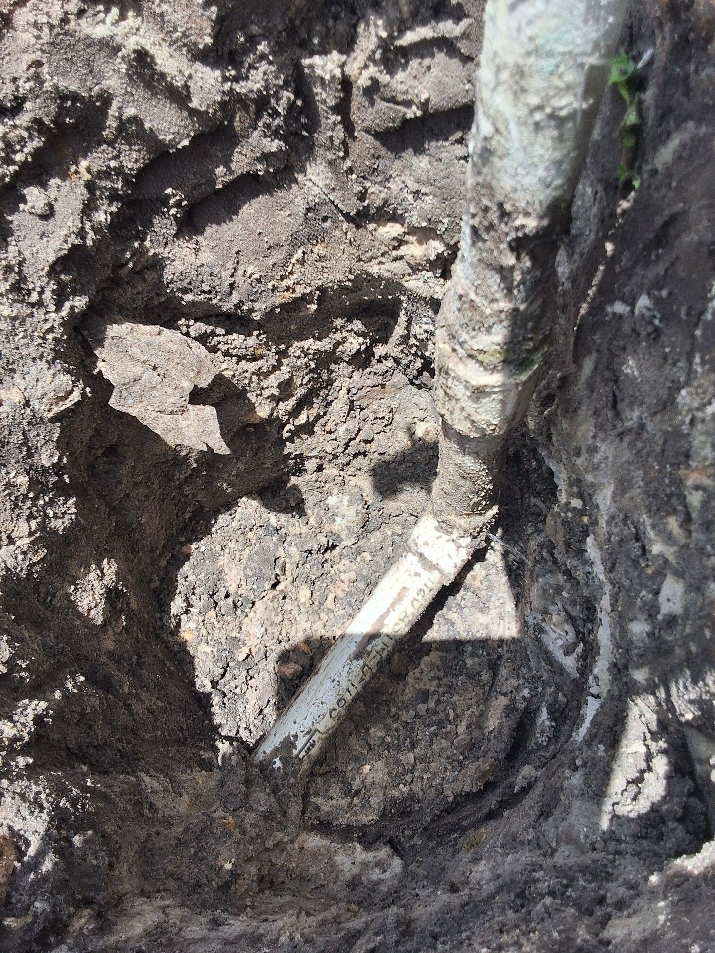 Mud-filled excavation with a white pipe or cable running vertically along the right side.