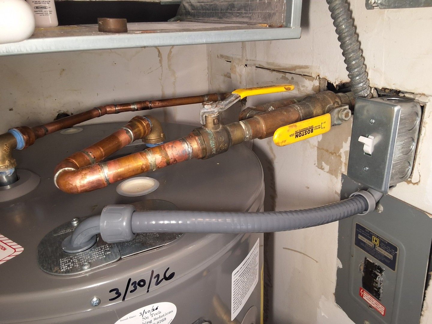 Copper pipes and yellow shutoff valves above a water heater in a utility closet