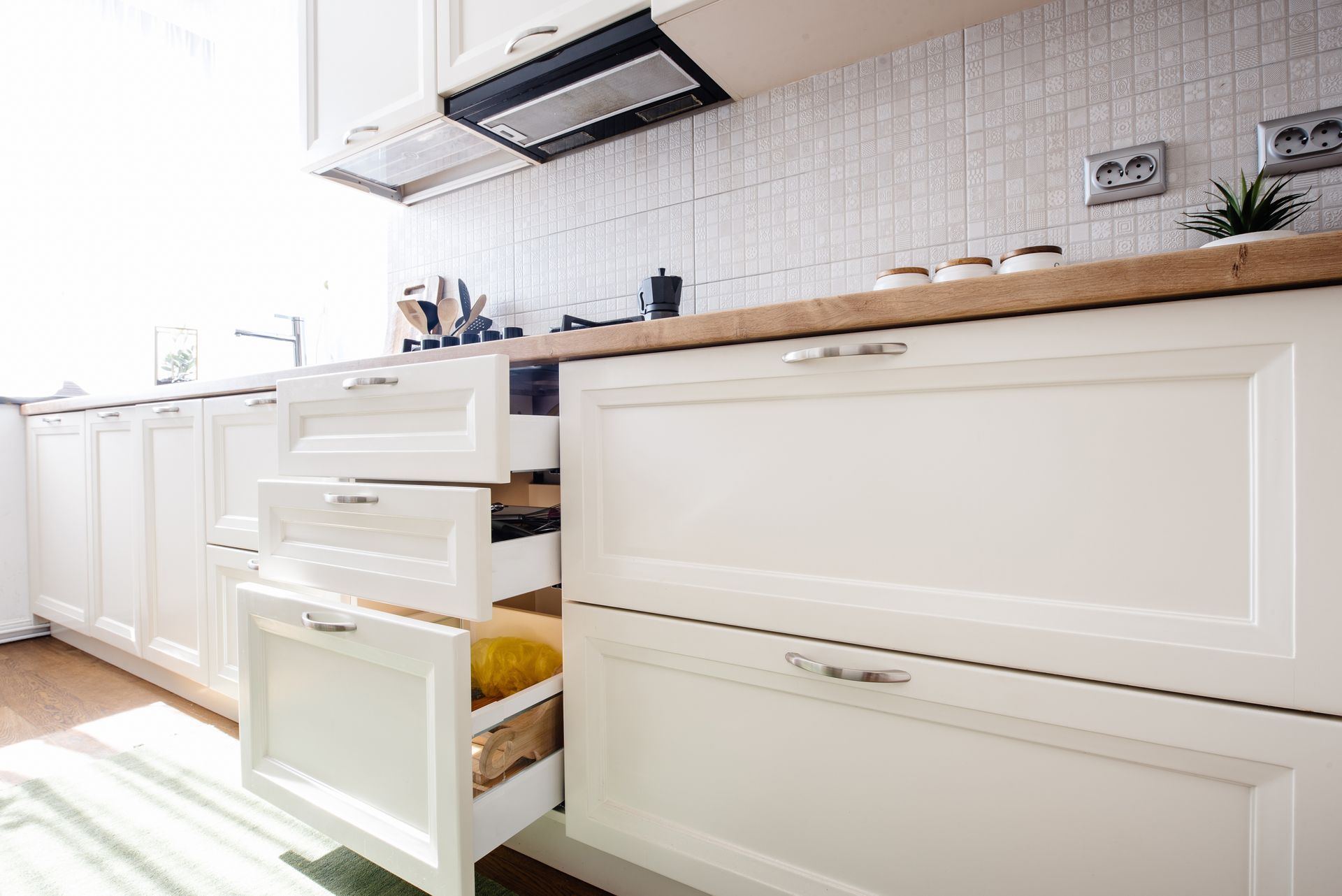 White kitchen with open drawers, cabinets, and light wood countertop beside a tiled backsplash