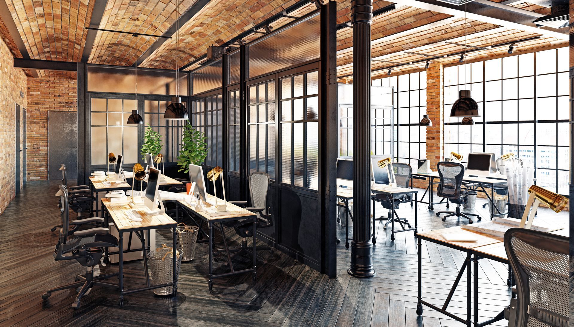 Bright industrial-style office with desks, chairs, and large windows under exposed brick and beams
