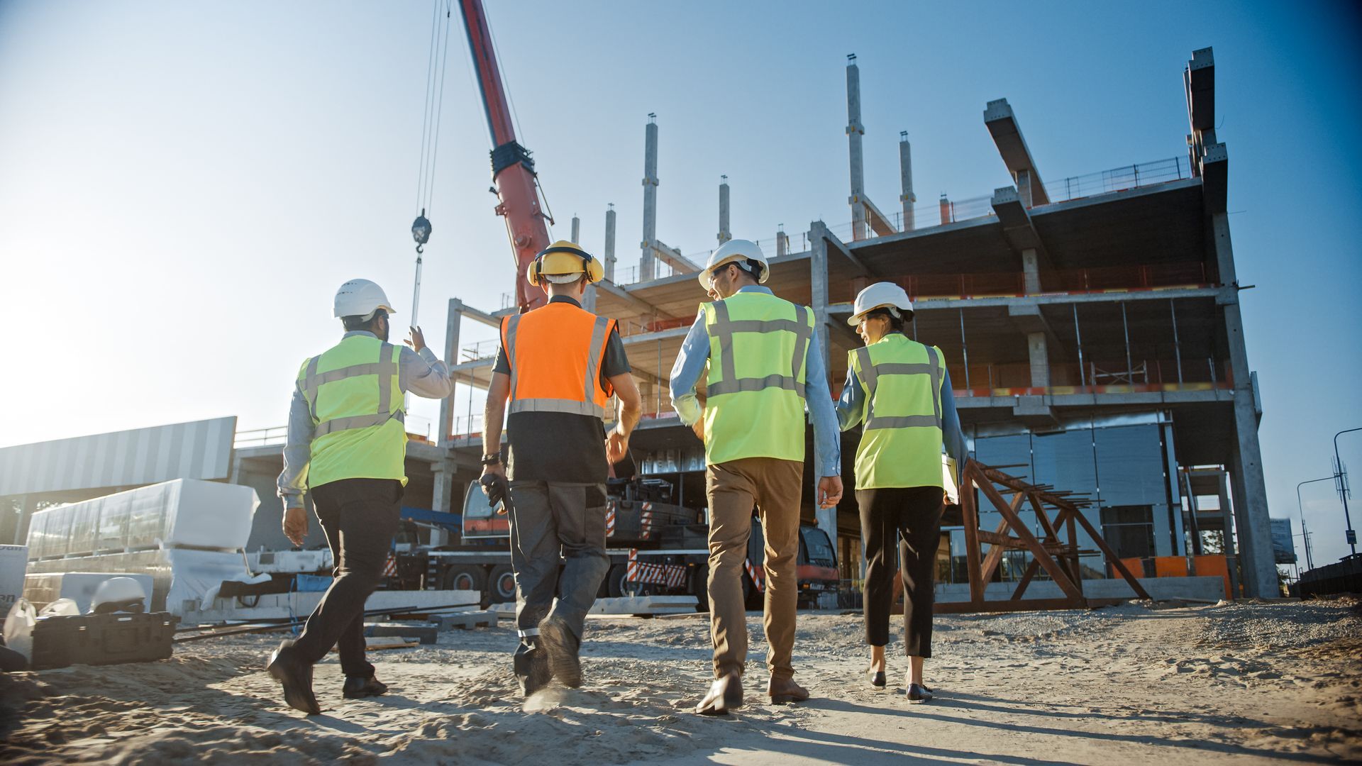 Construction workers in safety vests and helmets near a building frame with a crane on site
