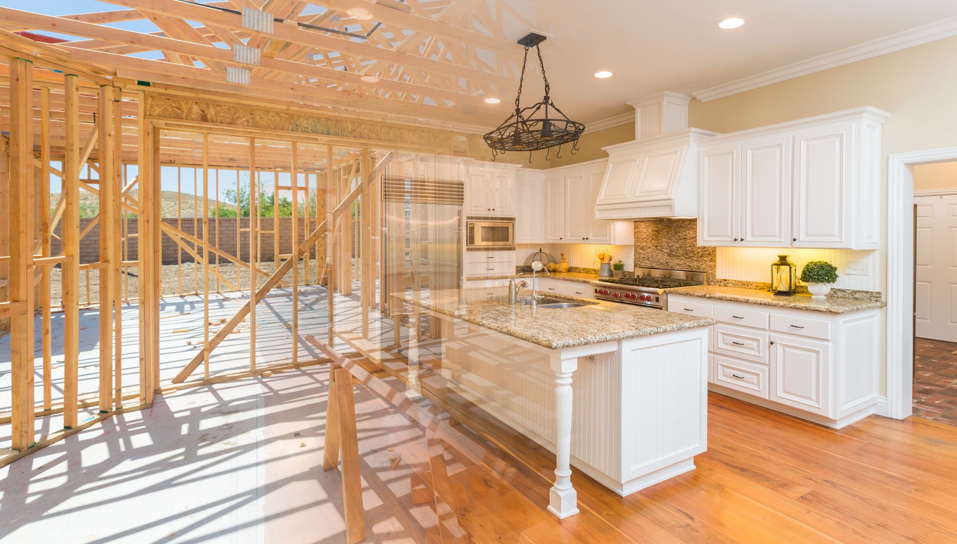 Bright kitchen under construction with exposed framing, white cabinets, granite island, and hardwood floors