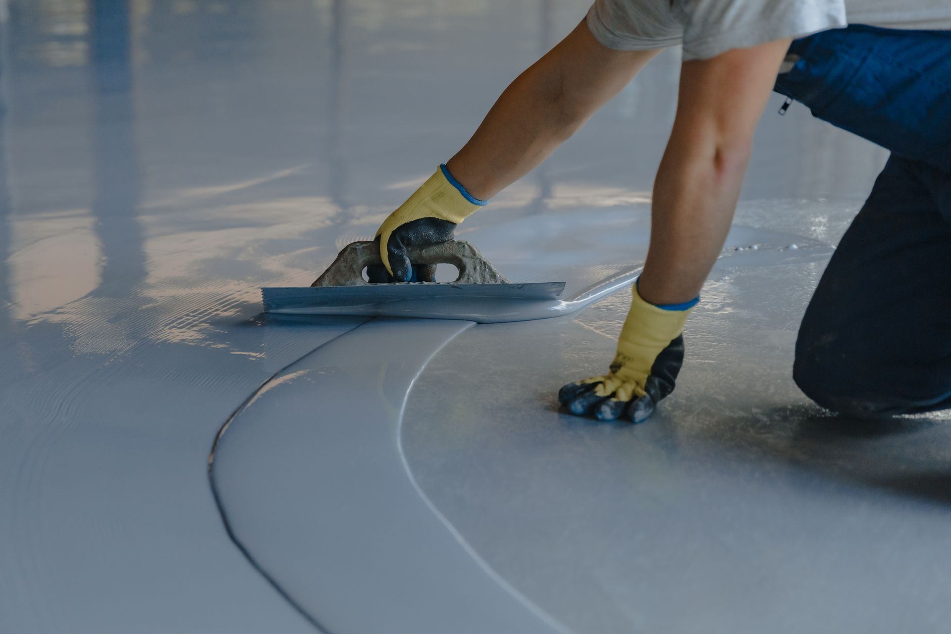 Worker smoothing a curved seam in a glossy floor with a trowel