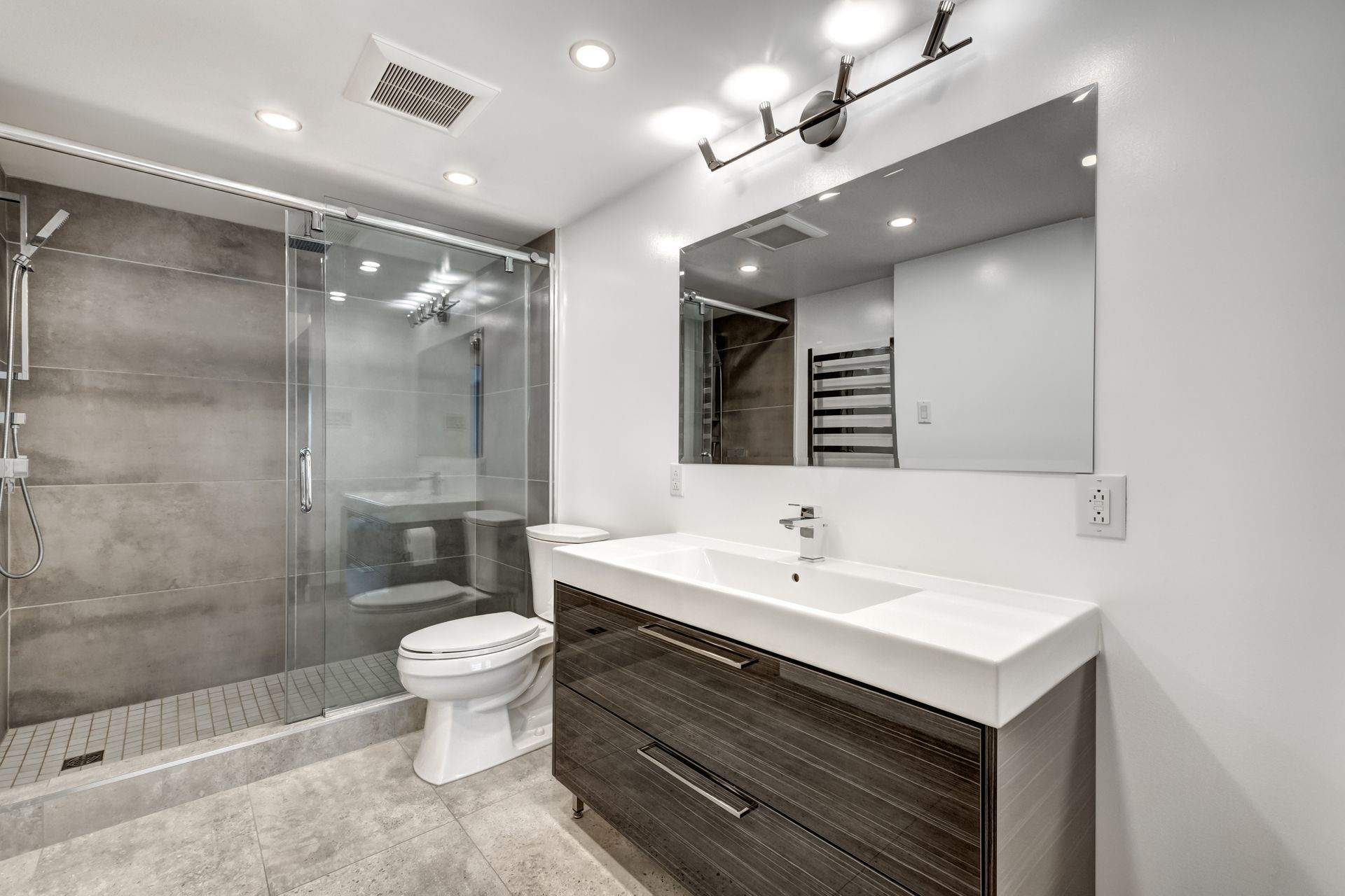 Modern bathroom with glass shower, toilet, floating vanity, large mirror, and gray tile flooring