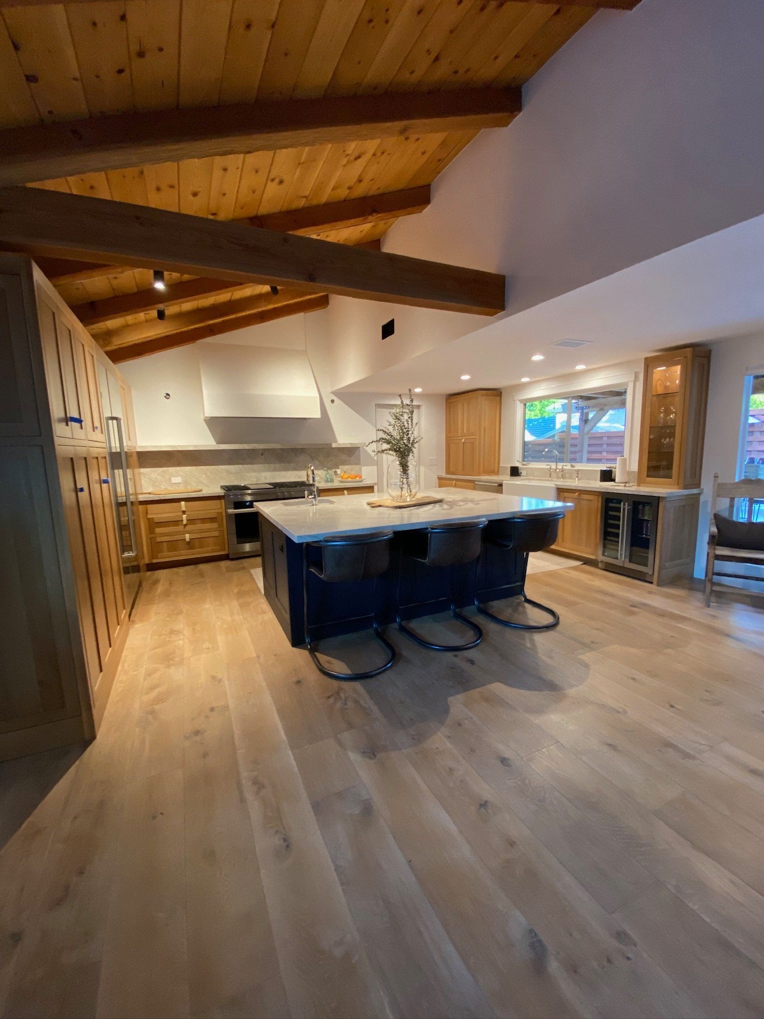 Modern kitchen with wooden ceiling, large island, and rustic cabinetry in a bright open-plan space
