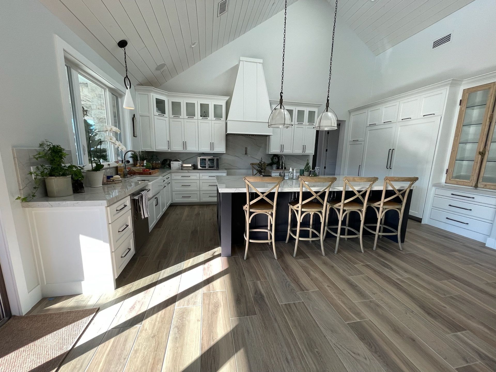 Bright modern kitchen with white cabinets, island stools, and wood-look flooring