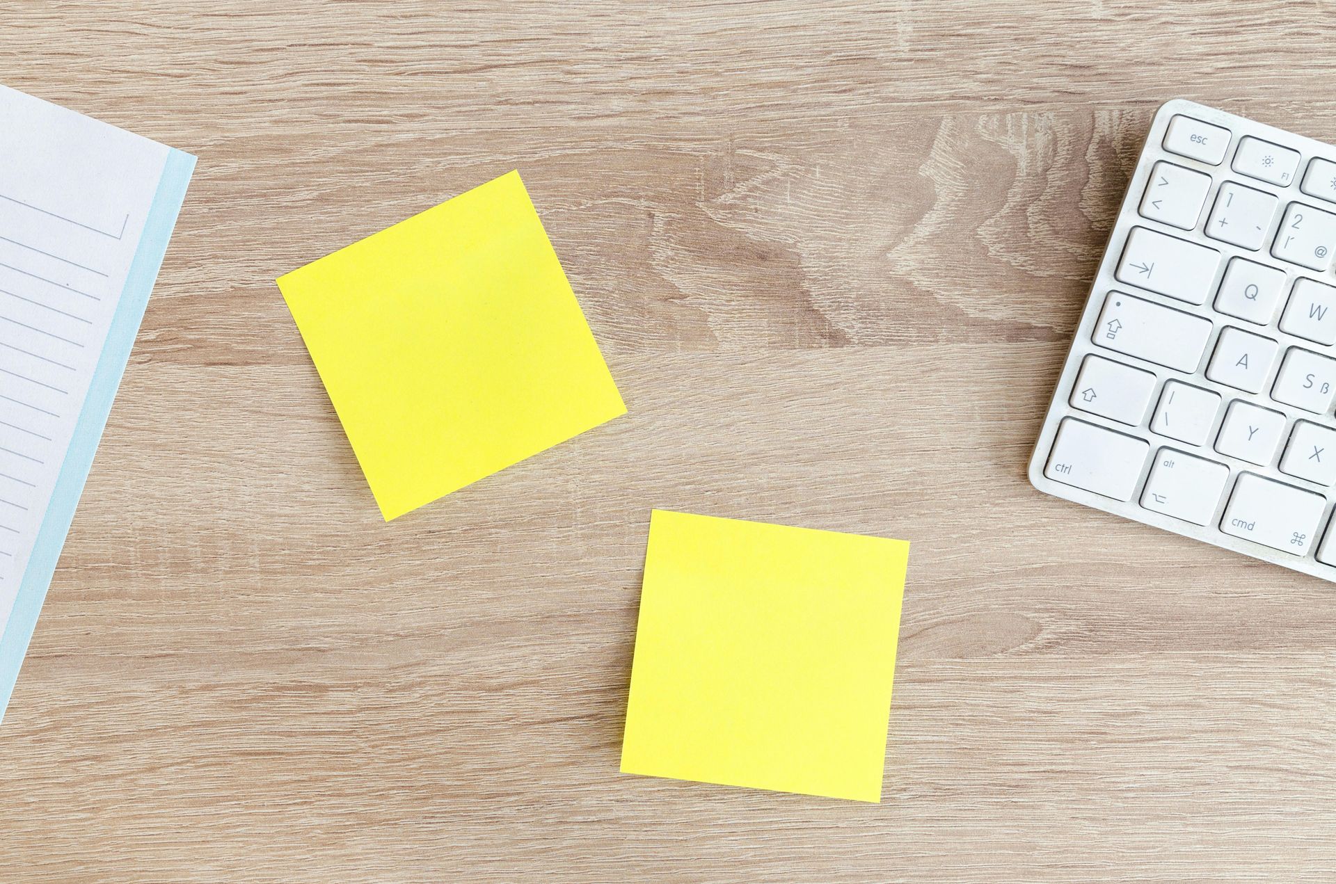 Three yellow sticky notes are sitting on a wooden table next to a keyboard.