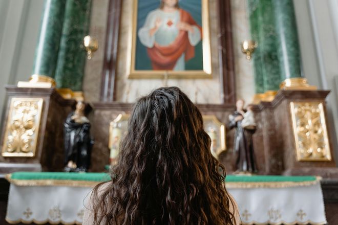 A woman is sitting in front of an altar in a church looking at a painting of jesus.
