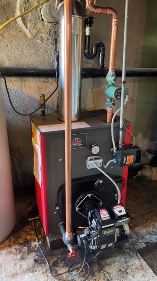 a red and black boiler is sitting in a basement next to a water heater .