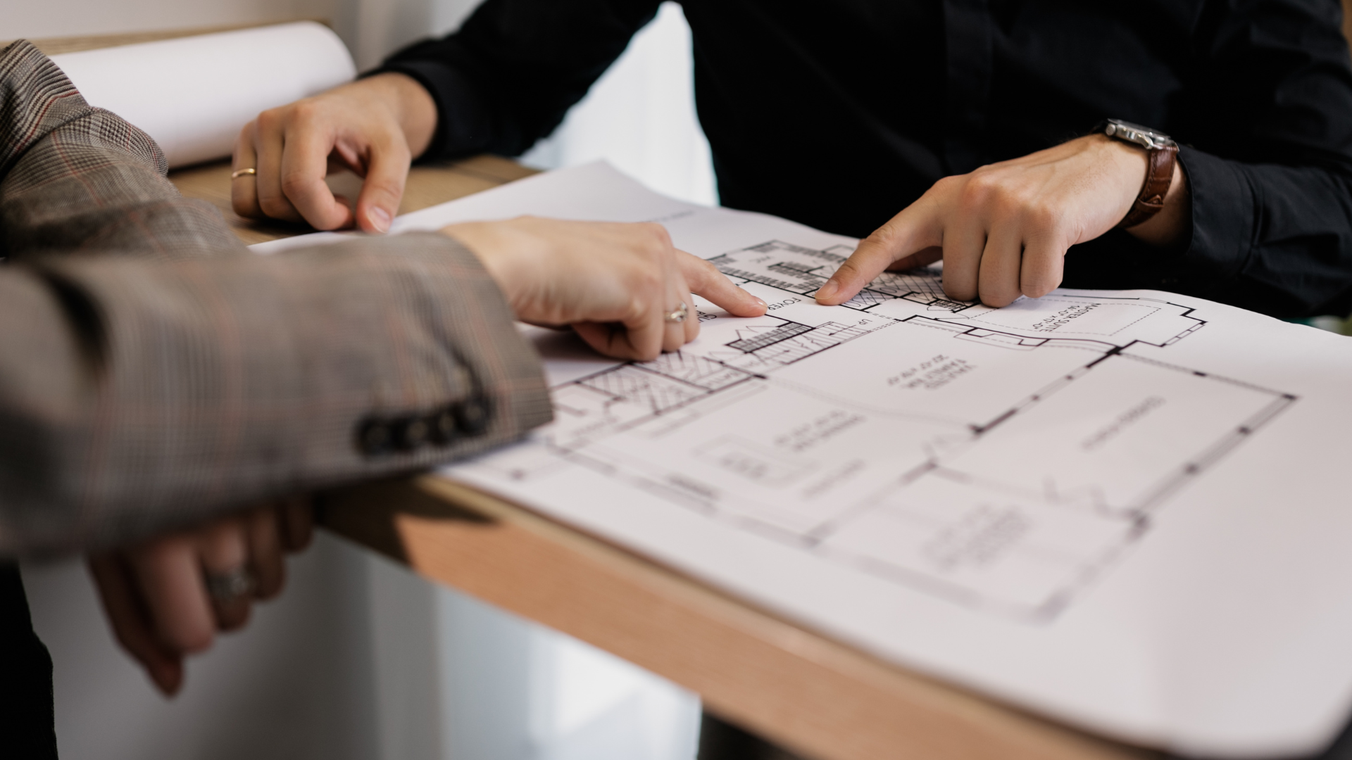 Two people are sitting at a table looking at a blueprint of a house.